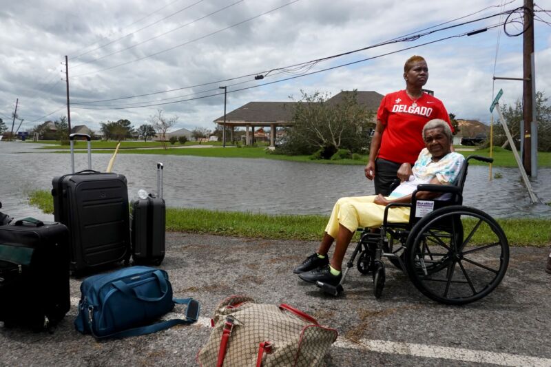 An elderly woman in a wheelchair and her daughter waiting for transportation in a flooded neighborhood.