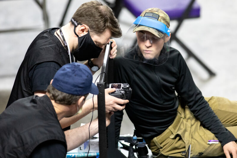 Men in face masks examine a digital camera.